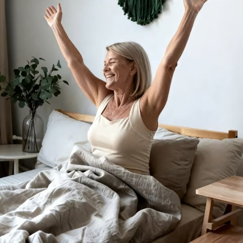 Eine Frau sitzt im Bett und streckt die Arme über den Kopf.