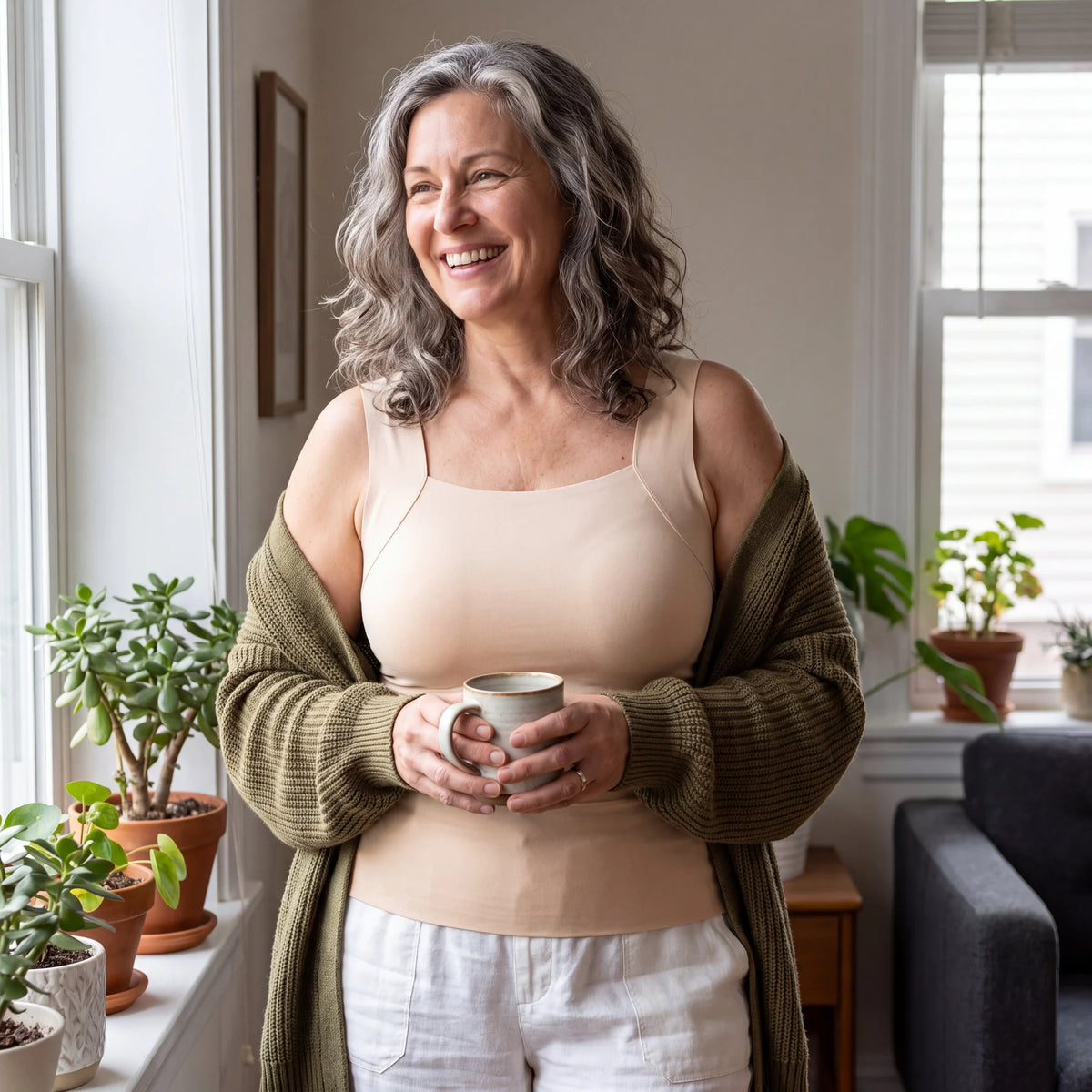 Eine Frau trägt das beige Top zu Hause unter einer Strickjacke.
